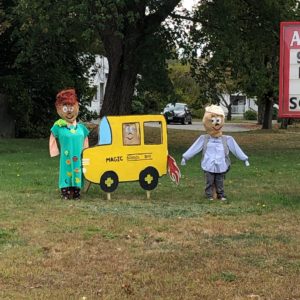 scarecrows dressed as "The Magic School Bus" characters standing near a cardboard school bus